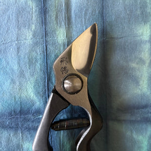 Close-up of Tobisho Hirei pruning shears blade tip and edge detail on blue washi paper