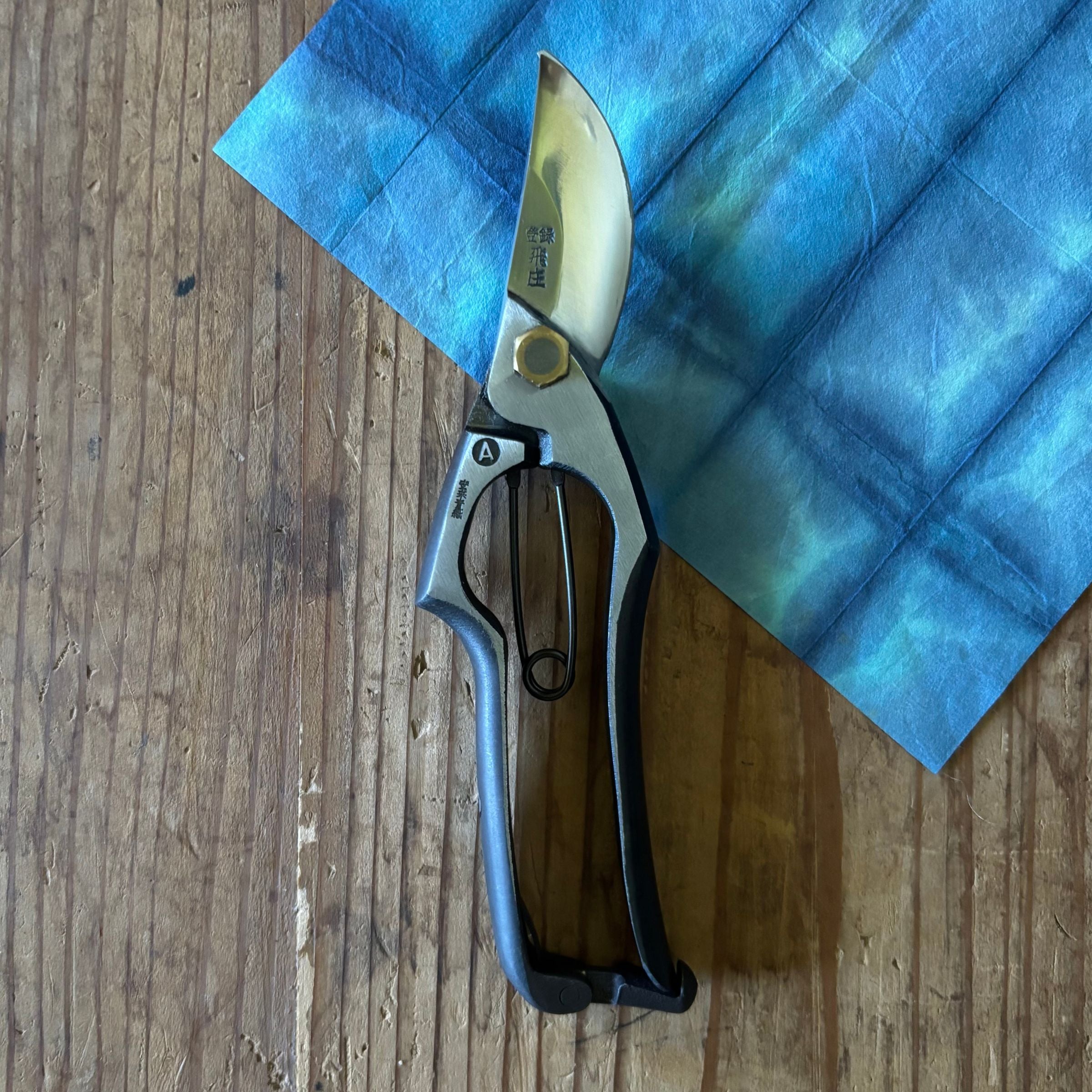 Close view of Tobisho Yasugi Blue Steel Type-A brazed pruning shears on indigo washi paper.