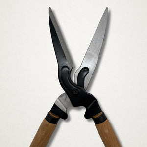 Japanese hedge shears with long timber handles, black forged body and polished blades, shown open against a white background