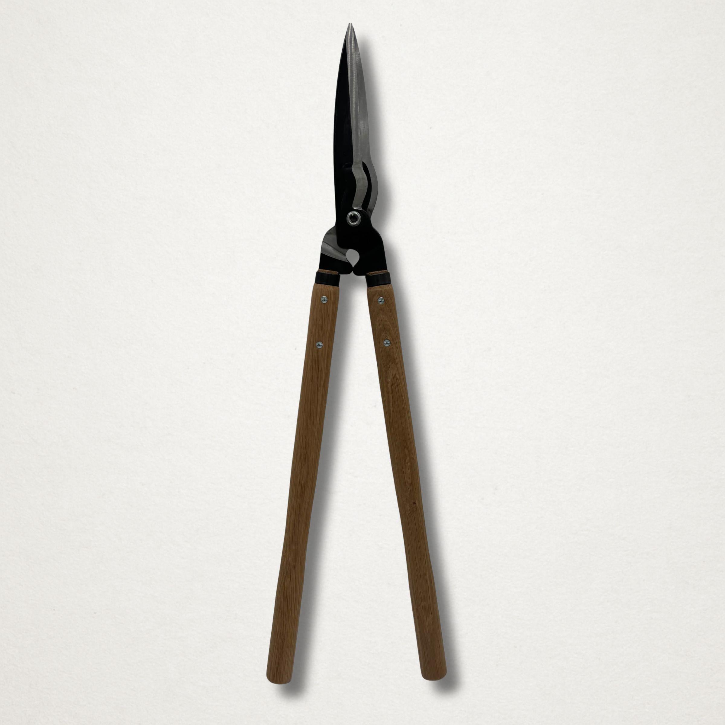 Full-length front view of Japanese hedge shears closed, with long wooden handles and black forged head on a white backdrop