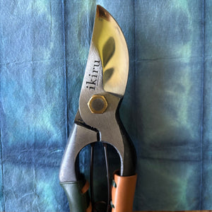 Ikiru secateurs closed on washi paper background – close-up of blades with engraved logo and leather handle grips.