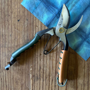 Ikiru secateurs open on washi paper background – angled photo showing blades apart, highlighting steel finish and joint details.