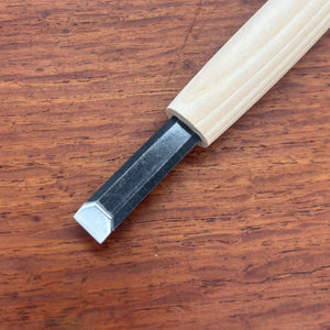 Close-up of a flat carving chisel from the Michi Hamono Little Jizo carving kit on a wooden board