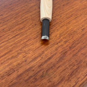 Close-up of a small rounded carving gouge from the Michi Hamono Little Jizo carving kit on a wooden board