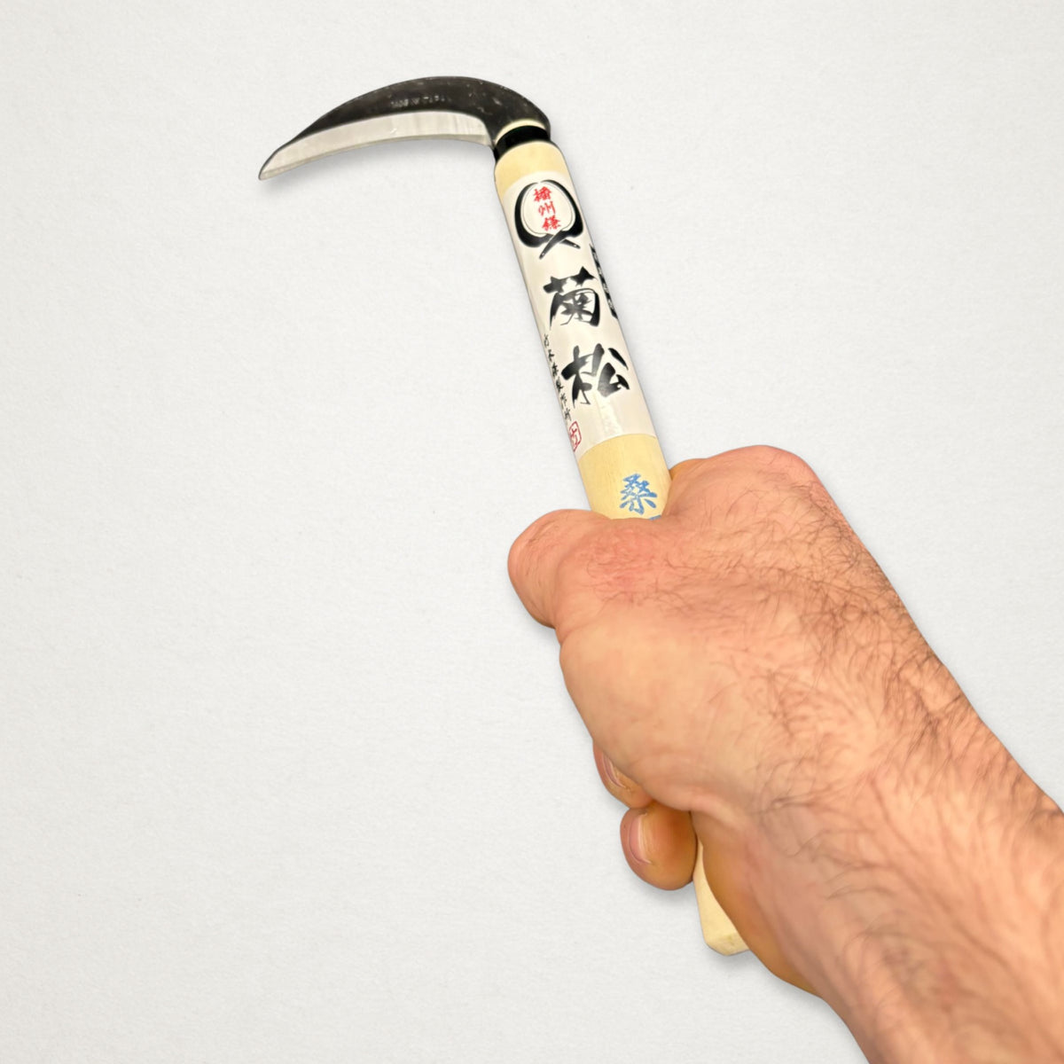 Hand holding Takemoto Kikumatsu mulberry sickle 90mm, showing compact handle and curved carbon steel blade