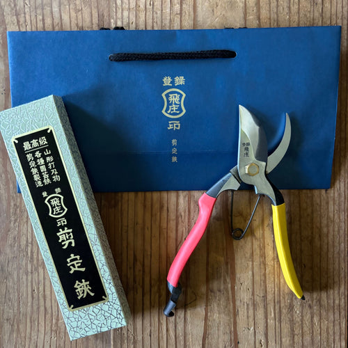 Tobisho SR-1 Japanese pruning shears beside box and blue bag, displayed closed on wooden surface
