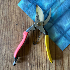 Tobisho SR-1 pruning shears open, showing blade curvature and red and yellow handles on blue washi paper