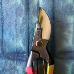 Tobisho SR-1 pruning shears positioned vertically on indigo washi paper with red and yellow handles visible