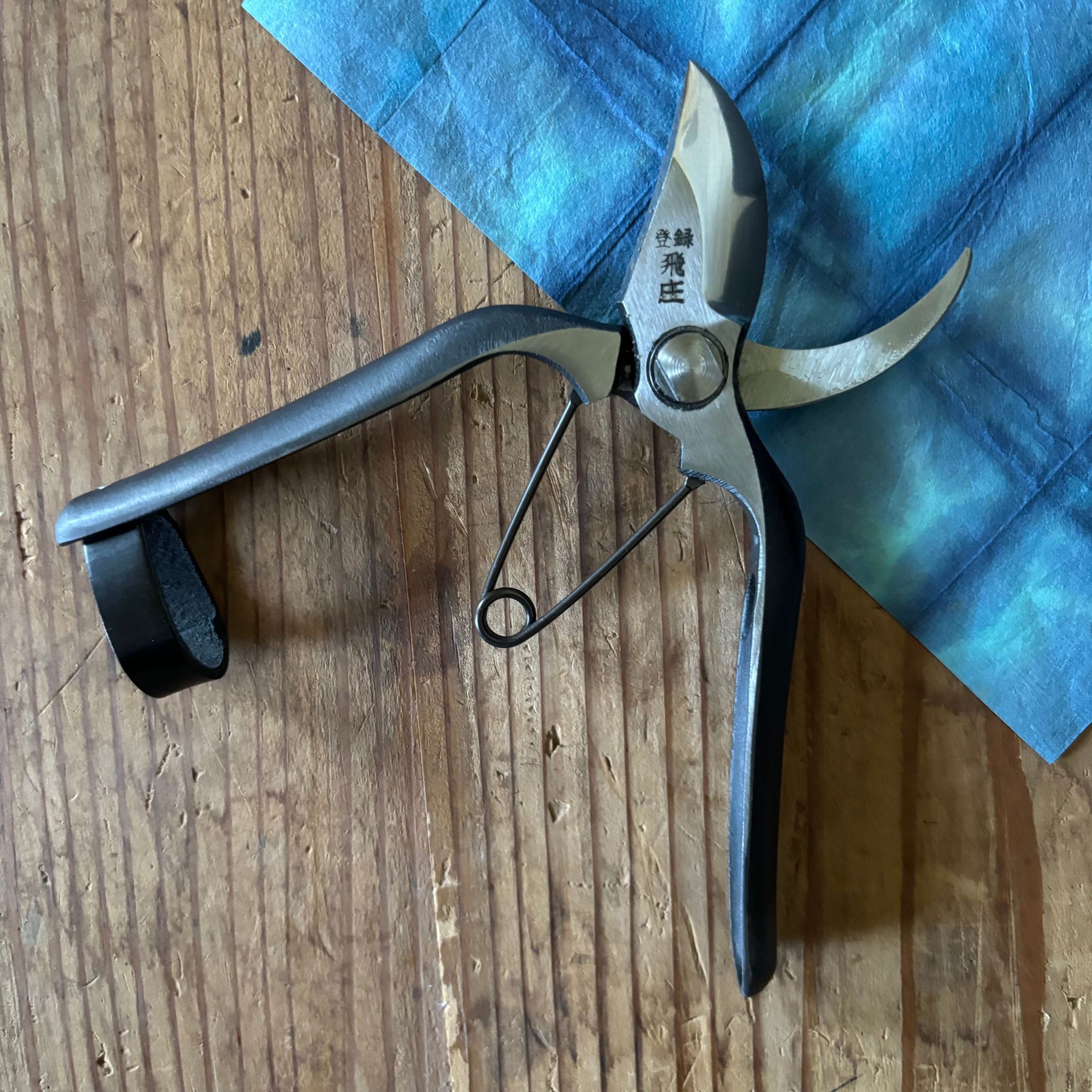 Tobisho Type-B 180mm Japanese pruning shears open on blue cloth background, Yasugi steel with upgraded leather strap lock