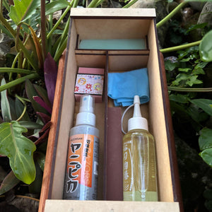 Japanese garden tool maintenance kit packed in a handmade wooden toolbox, with blade cleaner, camellia oil, cloth, rust eraser and sharpening stone in separate compartments.