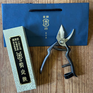 Tobisho pruning shears beside box and branded blue bag, presented on wooden surface