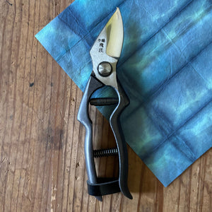 Tobisho pruning shears closed, displayed vertically on indigo-dyed washi paper background