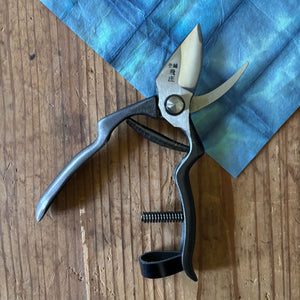 Tobisho pruning shears open, showing blade curvature and cutting action on blue washi paper