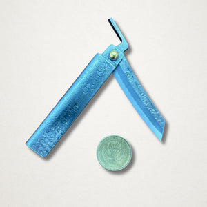 Japanese higo knife with hammered blue steel handle and partially open blade beside a one dollar coin on white background