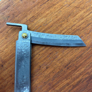 Close side view of a Japanese higo knife opened to ninety degrees, showing blade engraving and folded lever