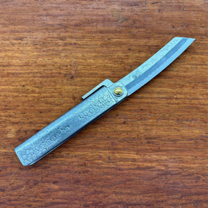 Japanese higo knife partially opened, showing hammered metal handle and angled blade on a timber tabletop