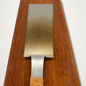 Front view of a Japanese saw resting on timber board showing blade shape and rattan-wrapped handle