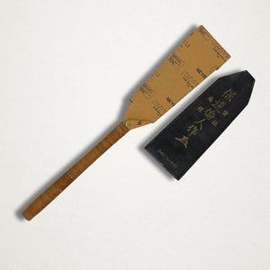 Japanese saw with paper blade sleeve and black protective sheath laid flat on white background