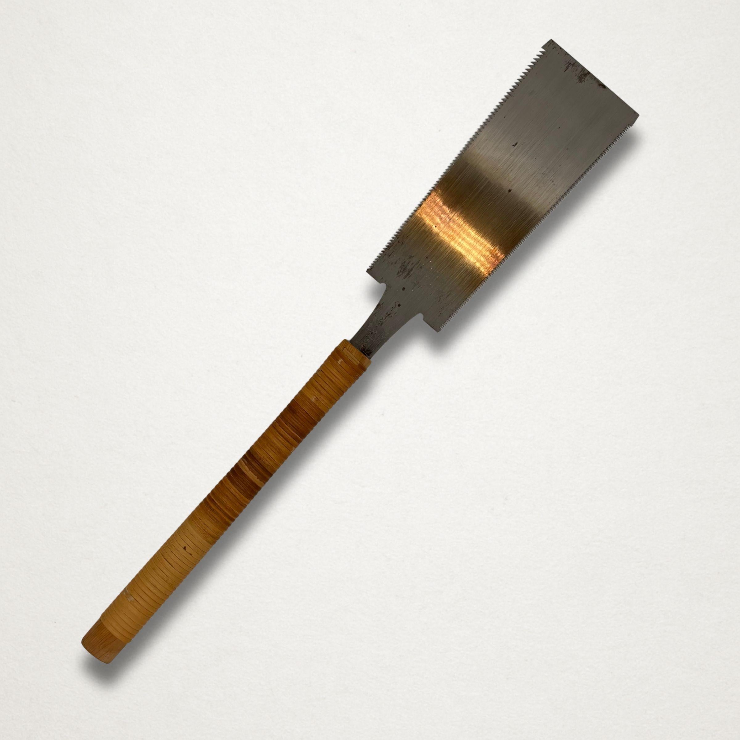 Vintage Japanese ryoba saw hanging vertically against a white background, showing full blade and cane-wrapped wooden handle