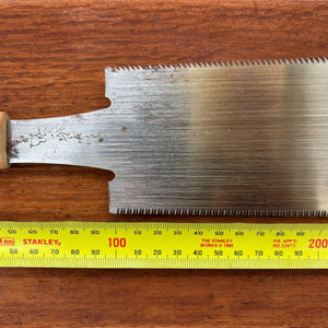 Close-up of a vintage Japanese ryoba saw blade beside a tape measure, showing tooth pattern, maker’s mark and blade width