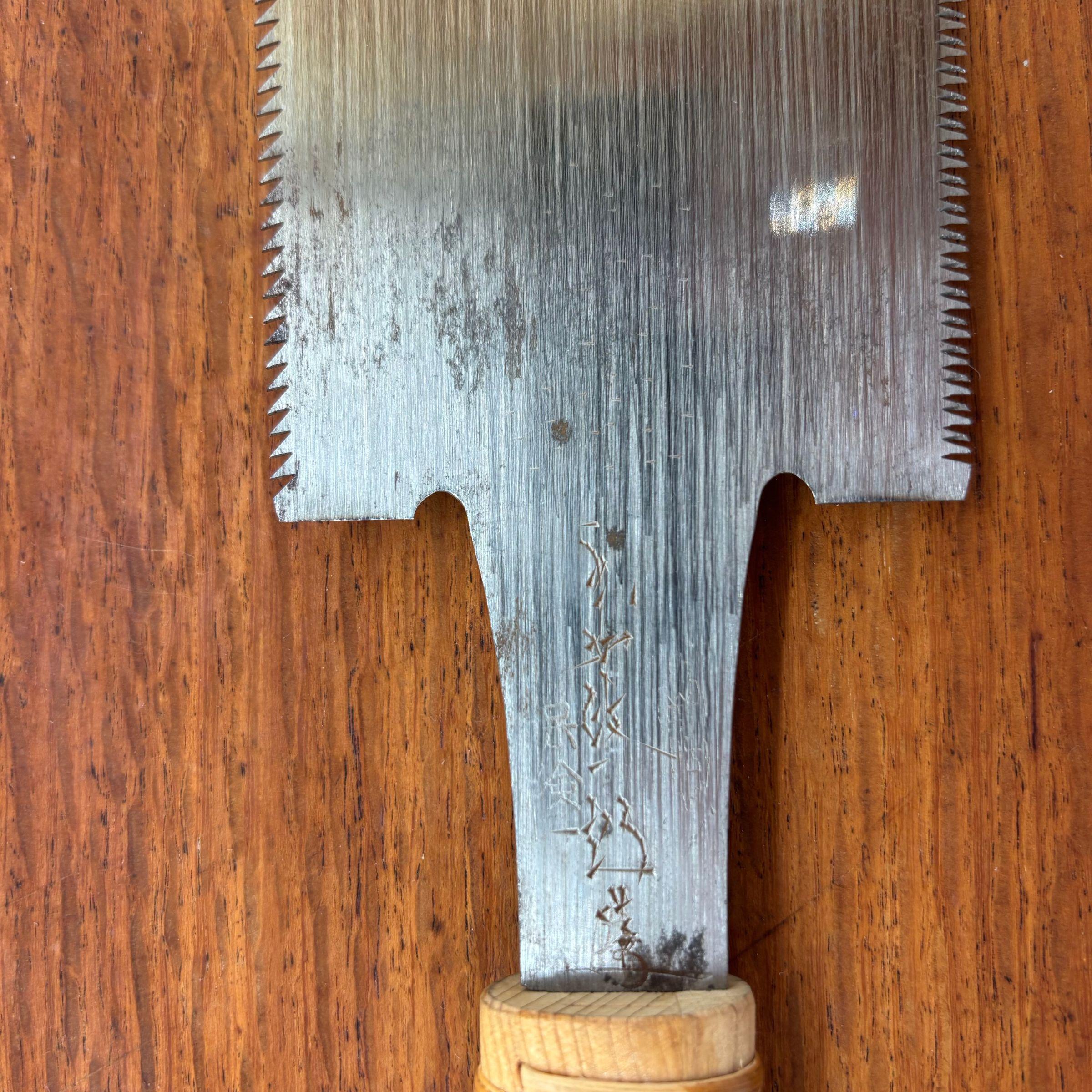 Close-up of the neck of a vintage Japanese ryoba saw showing engraved maker’s mark, patina and cane-wrapped handle collar