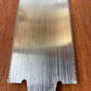 Close-up of the lower section of a vintage Japanese ryoba saw blade showing straight grain lines, light spotting and twin edge teeth