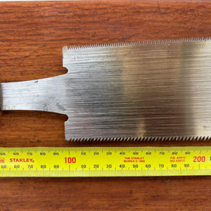 Close-up of the reverse side of a vintage Japanese ryoba saw blade beside a tape measure, showing blade width and tooth profile