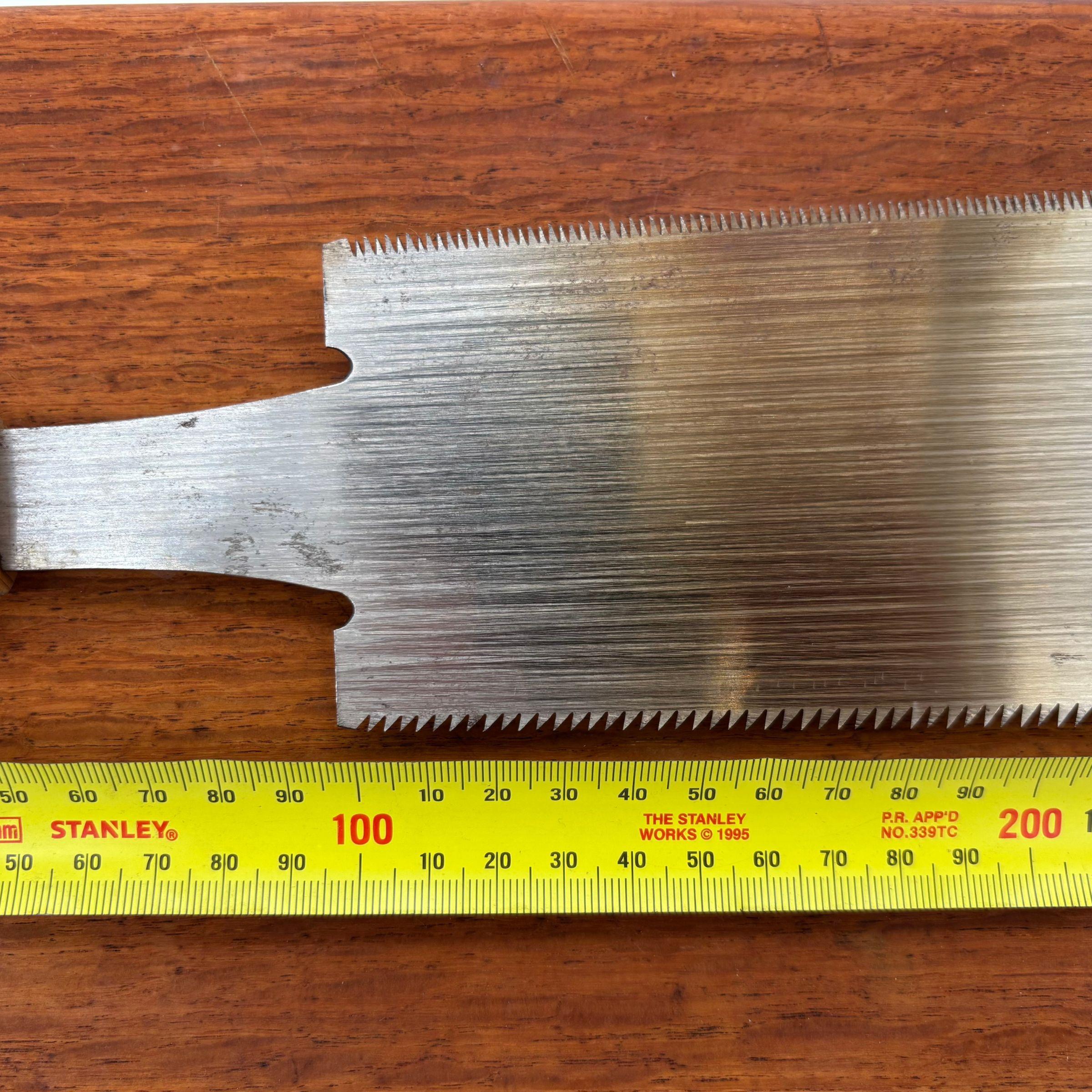 Close-up of the reverse side of a vintage Japanese ryoba saw blade beside a tape measure, showing blade width and tooth profile