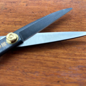 Black Japanese tailor scissors with blades open, close-up side view on timber surface